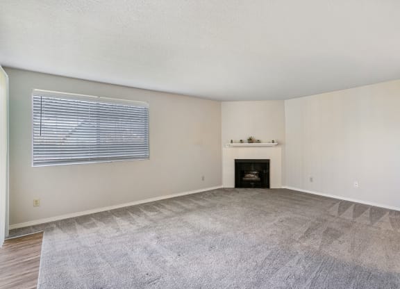 Spacious living room with gray carpet, fireplace, and mantle in the center, and an entrance to outside on the left. at Capitol Crossing, Olympia, WA 98501