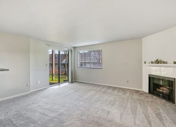 Carpeted living room, gas fireplace, and mantle in the center, with a window and sliding glass doors to a grass lawn.at Capitol Crossing, Olympia, WA