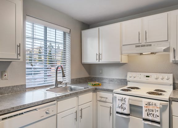 Kitchen with white cabinets, a window above the sink, and a white stove top and oven with staged hand towels.at Capitol Crossing, Olympia, Washington
