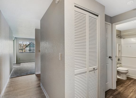 Wood floor hallway with access to living room and kitchen, shutter door closet, linen closet, and bathroom from left to right.at Capitol Crossing, Olympia, 98501