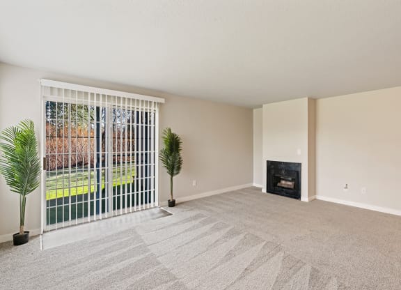 Living room with two plants beside sliding glass doors with panel blinds to grass lawn, and a gas fireplace on back right wall.at Capitol Crossing, Olympia, Washington