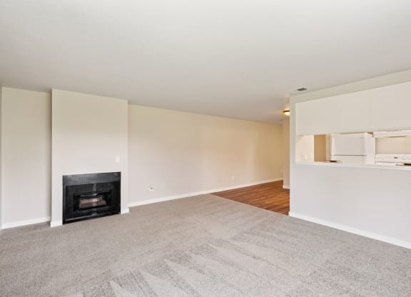 Living room with gray carpets, black gas fireplace, and light-colored walls leading to kitchen.at Capitol Crossing, Olympia, 98501