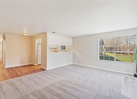 Spacious living room, window with a view of grass and trees, wood floor hallway past kitchen flowing to bedroom on the left.at Capitol Crossing, Olympia, WA