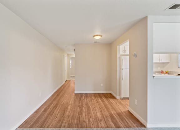 the living room and kitchen of an apartment with a hard wood floor and white walls