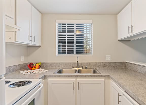 U-shaped kitchen with gray countertops, a window centered above stainless steel sink, and a bar-style counter on left.at Capitol Crossing, Washington, 98501