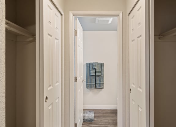 Hallway with sliding door closets on either side leading to bathroom staged with bathmat and towelsat Capitol Crossing, Olympia, WA.