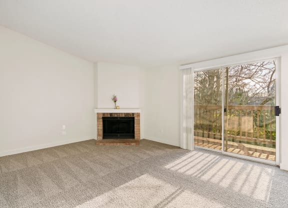 A large carpeted living room with white walls, a fireplace, and sliding glass doors to a private balcony with nature views. at Pointe East, Washington, 98424