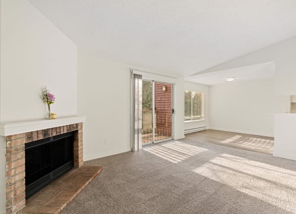 A Pointe East Apartments living room with carpet, a brick fireplace, access to a balcony, and a view of the dining room behind. at Pointe East, Washington, 98424