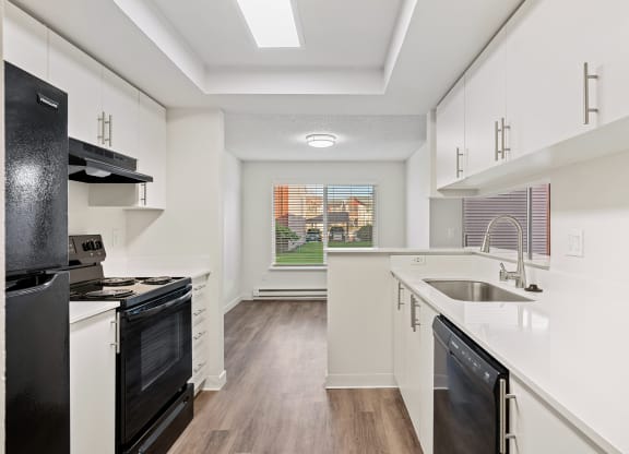 A galley-style kitchen with white countertops and cabinets looks into the dining room with a large window and a view of a grass lawn. at Pointe East, Washington