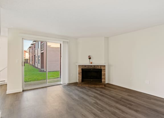 A living room with wood flooring, a brick fireplace and sliding glass doors. at Pointe East, Fife, Washington