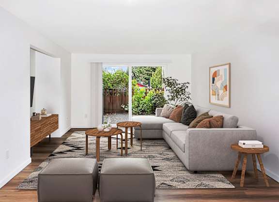A living room with a grey couch, a wooden coffee table, and a large window with a view of a garden at Heritage Woods Apartments in Renton.