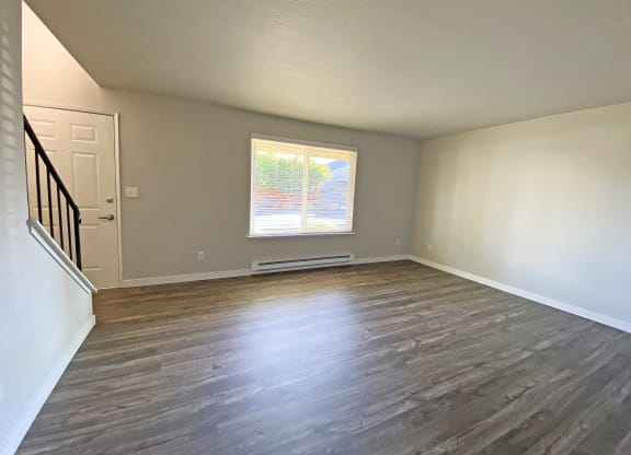 Spacious living room with large window, wood-style flooring, front door, and stairs to the right.at Quilceda Gardens, Washington