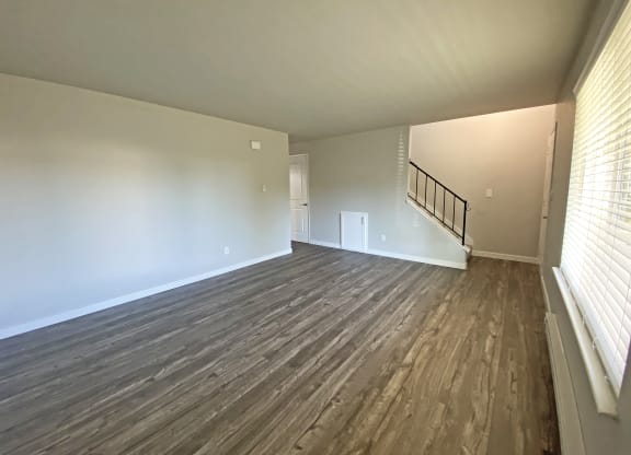 Large living room with faux wood flooring, a large window on the right wall, and an upstairs stairwell on the back wall.at Quilceda Gardens, Marysville, Washington