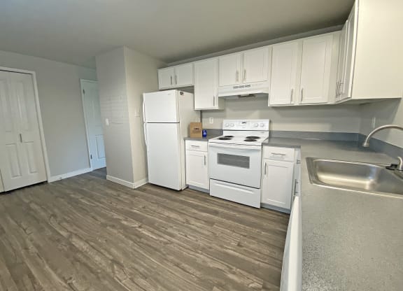 L-shaped kitchen with white appliances, top and bottom cabinets, wood-like flooring, and closet.at Quilceda Gardens, Marysville, WA