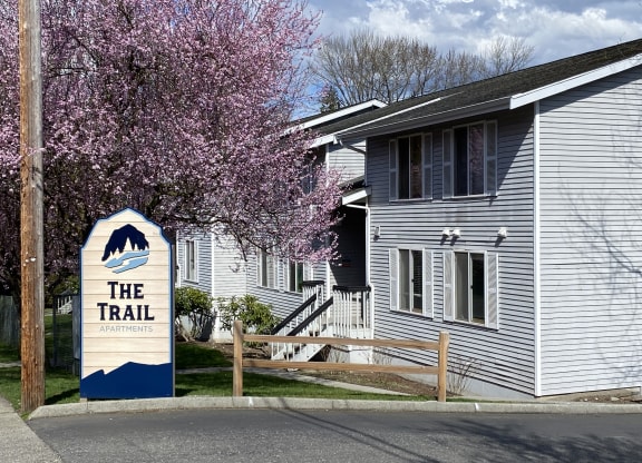 the Trail Apartments sign in front of a white building with a cherry tree in the foreground.at The Trail, Washington