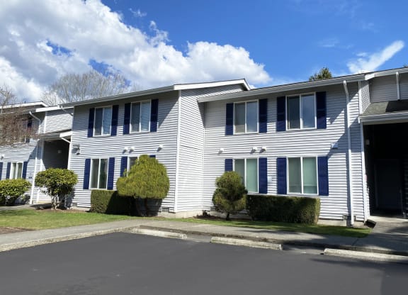 Outside apartments with a paved pathway surrounded by green grass, and well-maintained landscaping.at The Trail, Washington, 98290