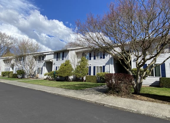 Apartments with grass yards in front, landscaping, trees and a paved walkway. Blue skies are behind the apartments.at The Trail, Snohomish, WA 98290