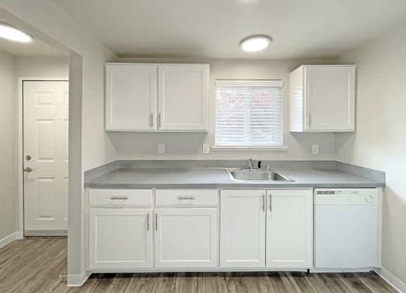 Light-filled kitchen with white cabinets and appliances, a window above the sink, and wood-like flooring.at Quilceda Gardens, Washington