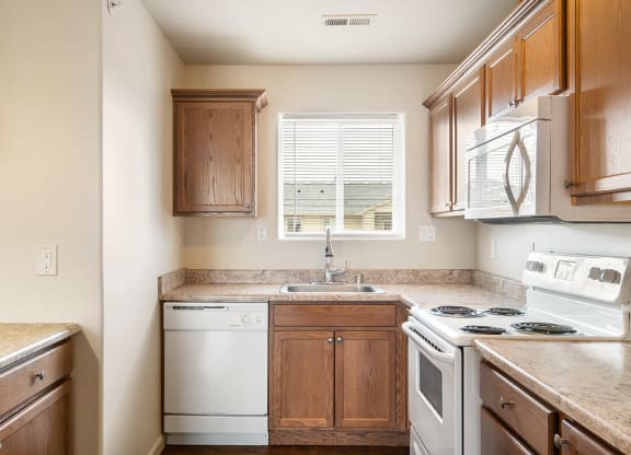 L-shaped kitchen with breakfast bar to the left and white appliances including a dishwasher, stove, oven, microwave, and sink with window above. at Pine Tree Park, Washington