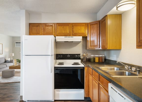 A side view of the kitchen with a white full-size refrigerator next to a stovetop oven and wood cabinets.at Wildflower, Kennewick, 99336