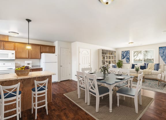 Kitchen opens up to the dining area and living room. Staged with dining set, couch, two chairs, wall bookshelf, and rugs. at Pine Tree Park, Washington