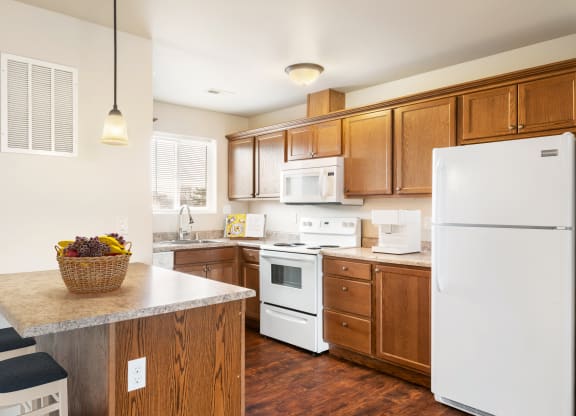 L-shaped kitchen with top and bottom cabinet storage, white appliances, and a breakfast bar staged with bar stools. at Pine Tree Park, Kennewick