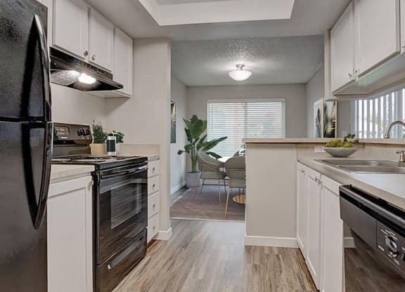 A kitchen with a full-size fridge, oven, stovetop, double bowl sink, and dishwasher. White top and bottom cabinets and a breakfast bar. at Pointe East, Fife, Washington