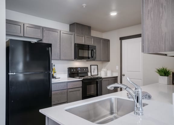 Kitchen with white countertops and grey cabinets. Kitchen has black fridge, black stove and oven, black microwave and stainless steel sink. at Altitude, East Wenatchee, WA, 98802