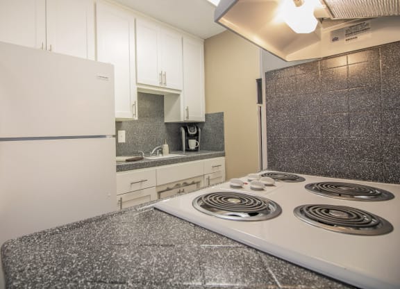 Galley kitchen with new white cabinets and gray faux granite countertops, with dining area visible in the distance  at Woodland Village Apartments , Woodland, CA 95695