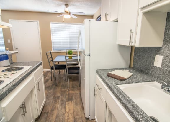 Galley kitchen with new white cabinets and gray faux granite countertops, with dining area visible in the distance at Woodland Village , California, 95695