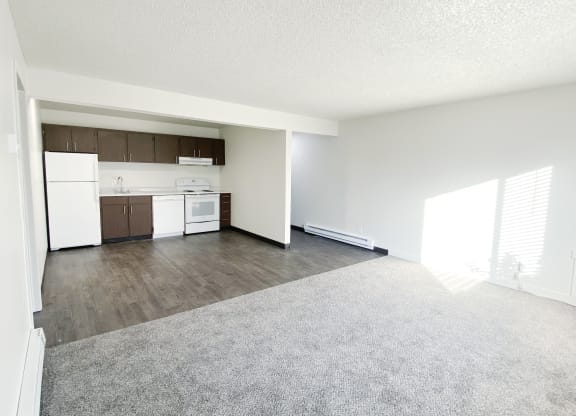 Open living room looking into dining area and galley kitchen with wall dividing hallway. White appliances, cabinet storage.at Laurel Park, Twin Falls, 83301