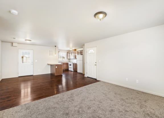 The living room has white walls and a gray carpet that meets hardwood floors in the dining area and kitchen. at Pine Tree Park, Kennewick