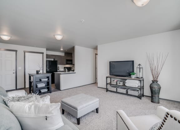 Large carpeted living showing a chair, couch, tv and plant. Open floor plan from dining room and kitchen. Hallway off of living to bedrooms. at Altitude, East Wenatchee, WA