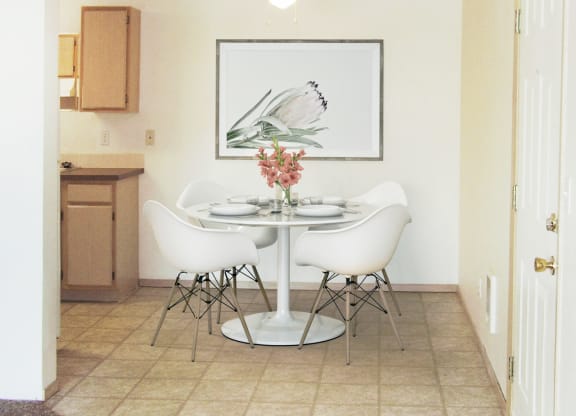 Dining area with ceiling fan, and the kitchen to the left. Staged with a table, 4 chairs, wall art, and flowers.at North Pointe, Post Falls Idaho