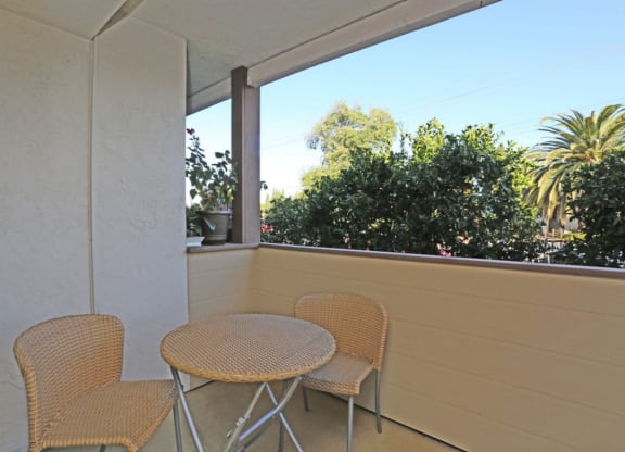 Apartment private patio with small table and two chairs overlooking trees on a sunny day at Pacific Sands, California, 92117