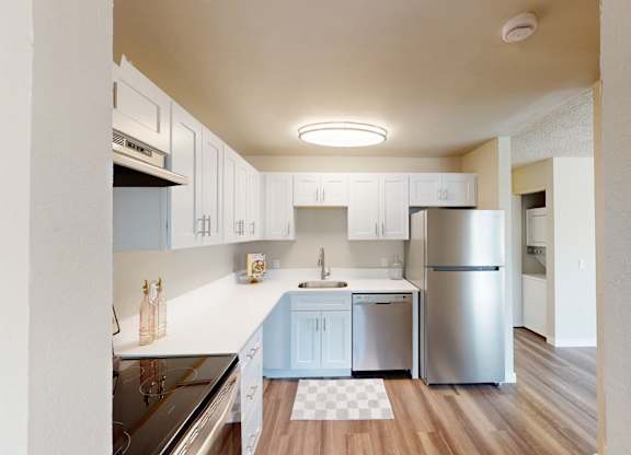 Contemporary kitchen at Peak 88 Apartments Renton WA with sleek white cabinets, stainless appliances, and wood-style floors.