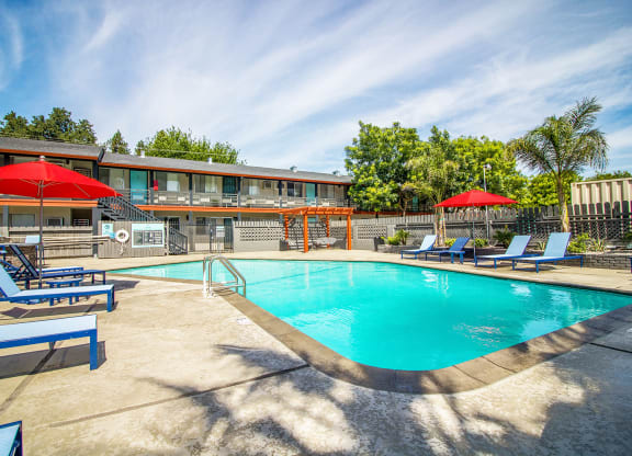 Woodland Village pool with blue lounge chairs, red umbrellas and landscaping.at Woodland Village Apartments , Woodland
