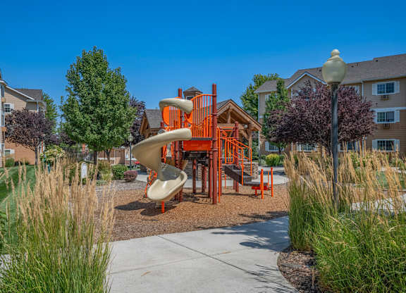 A playground with a slide and a play structure in the middle of a grassy area.