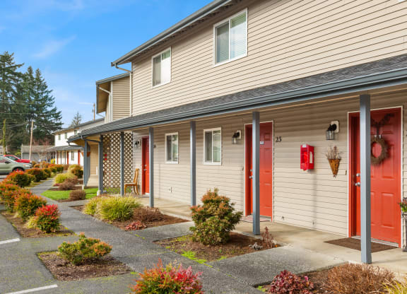 Outside apartments with red doors and paved walkways with colorful landscaping leading to each door.at Quilceda Gardens, Marysville, WA