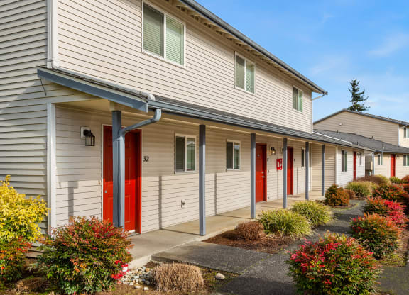 Apartment building exterior with a paved walkway lined with flowers and bushes.at Quilceda Gardens, Marysville, 98270