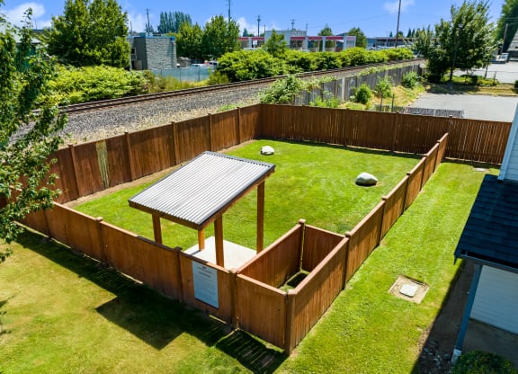 a dog park with large grassy area, covered section for shade and rain protection and rocks