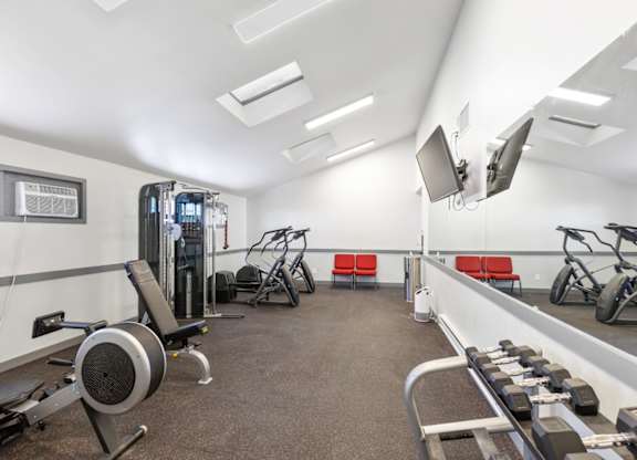 A gym with a variety of equipment including a weight bench, a rowing machine, and a treadmill.