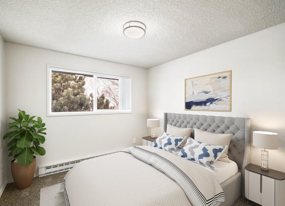 A bedroom with white walls, overhead lighting, and a window on the left wall. Staged with a bed, 2 side tables, a plant, and a rug.at Wildflower, Kennewick Washington
