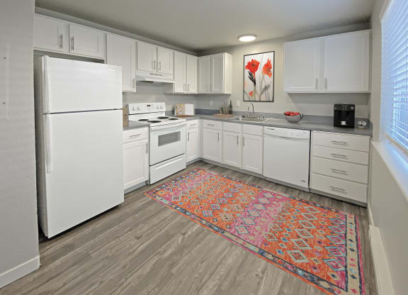 L-shaped kitchen with top and bottom cabinet storage, gray countertops, white appliances, and a large window on the right wall.at Quilceda Gardens, Washington
