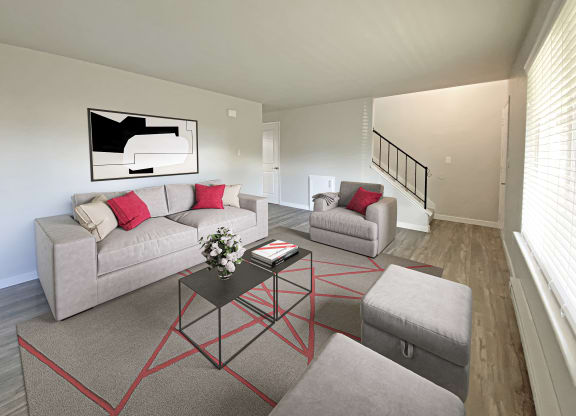 Living room with stairs on far wall and oversized window on the right wall. Staged with couch, chair, 2 ottomans, rug, and table.at Quilceda Gardens, Marysville, WA 98270