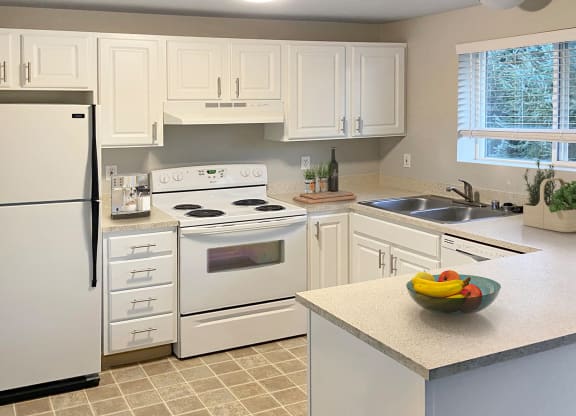 U-shaped kitchen with full-size fridge, stovetop and oven, sink with garbage disposal, dishwasher, and white cabinets.at Sitka Heights, Fife