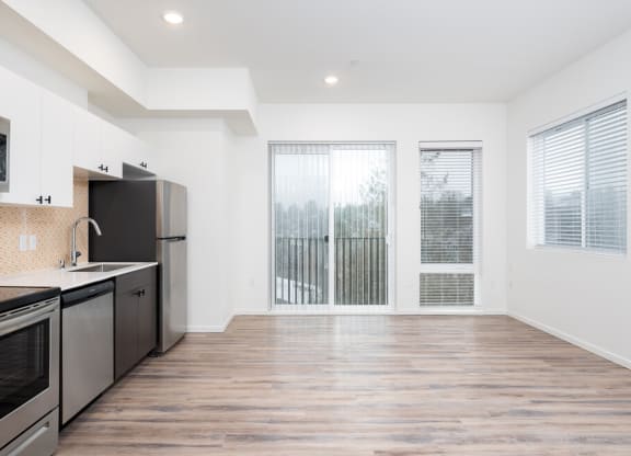 an empty living room with a kitchen and a window