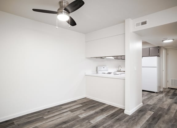 an empty living room with a kitchen and a ceiling fan