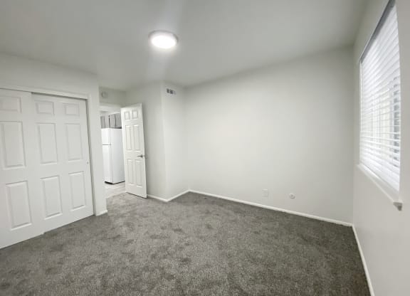 Bedroom with large sliding door closet, oversized window with white blinds on right, and door to hallway in back left corner at Summit, Pocatello, ID 83201