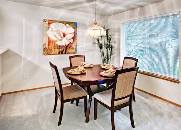 A dining room with a table set for two and a large painting on the wall.